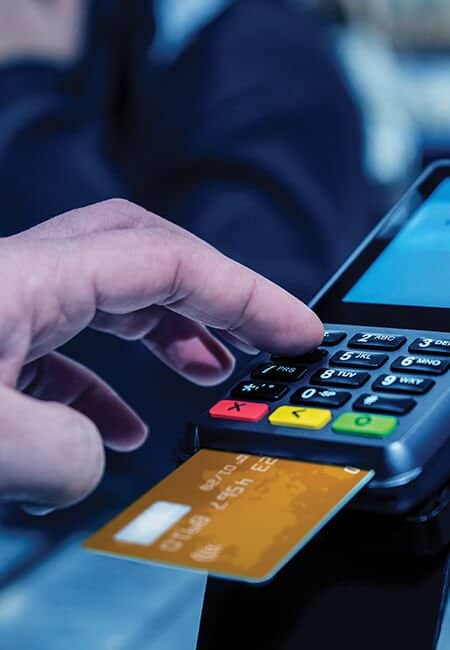 Close up of a chip card being put into a credit card terminal while the person types in their pin to finish up a transaction.